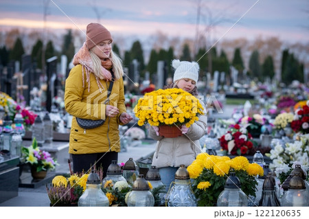 A mother and her child visit a beautiful flowered cemetery, honoring memories in autumn 122120635