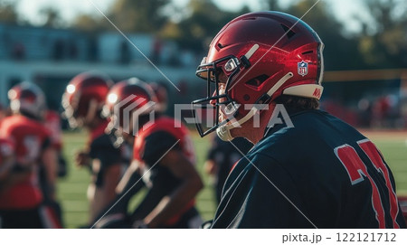 American football player in red helmet, waiting on the sidelines with his team during practice. 122121712
