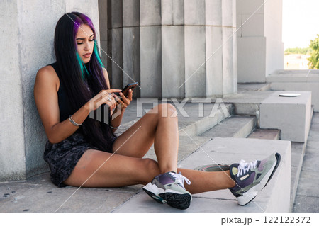 A young woman sitting with her cell phone on a staircase landing A young woman sitting with her cell phone on a staircase landing 122122372