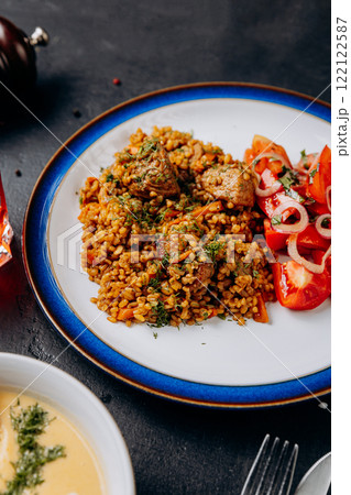 Savory bulgur pilaf with tender beef and fresh tomato salad,perfect for a hearty business lunch 122122587