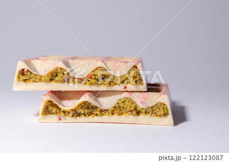 Trend white Dubai chocolate with pistachio, dried raspberry, tahini and kadaif, on white background, isolated, showing the filling. Confectionery and handmade sweets, chocolatier 122123087