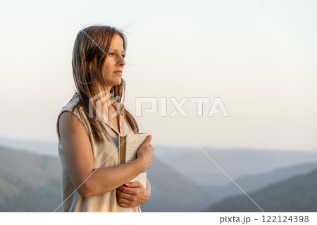 Woman with a book in mountain landscape during golden hour, showing tranquility and contemplation 122124398