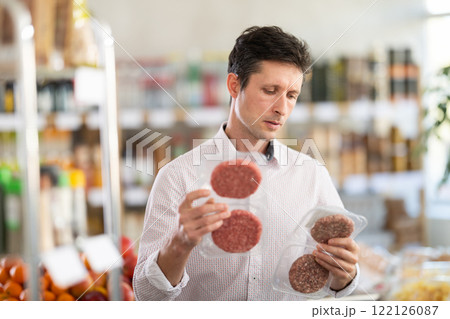 Man in light shirt choose and buy raw cooled semi-finished hamburger cutlet in store 122126087