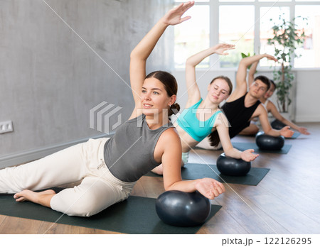 Young woman doing pilates exercises with softball under arm in training area 122126295