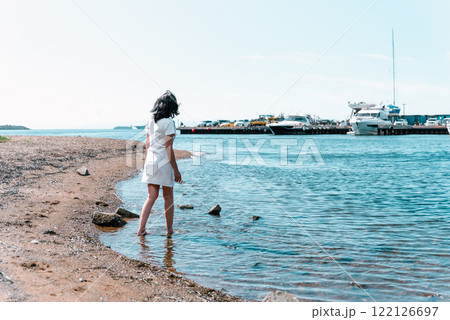 A 50-year-old Russian woman walking barefoot along the shore of the Sea of Japan in summer, with yachts and the pier visible in the background A 50-year-old Russian woman walking barefoot along the shore of the Sea of Japan in summer, with yachts and the pier visible in the background 122126697