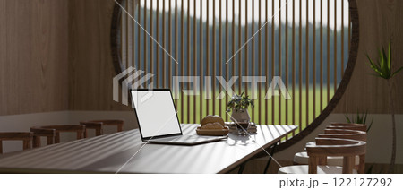 A laptop with a white screen mockup on a dining table in a cosy, minimalist Japandi dining room. 122127292