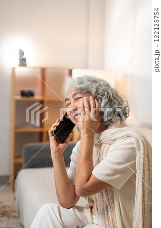 A happy, smiling Asian retired senior woman enjoys talking on the phone with her daughter. A happy, smiling Asian retired senior woman enjoys talking on the phone with her daughter. 122128754