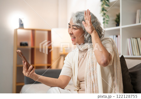 A cheerful Asian retired woman or grandma enjoys talking on a video call with her granddaughter. 122128755