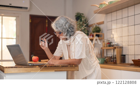 A positive, relaxed retired elderly Asian woman learns a new recipe from the internet in the kitchen 122128808