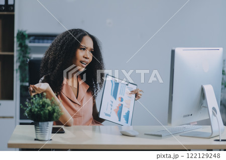 Female business person using digital tablet and laptop or remote working at home office, looking at digital tablet watching webinar, learning training, studying online seminar or video calling. 122129248