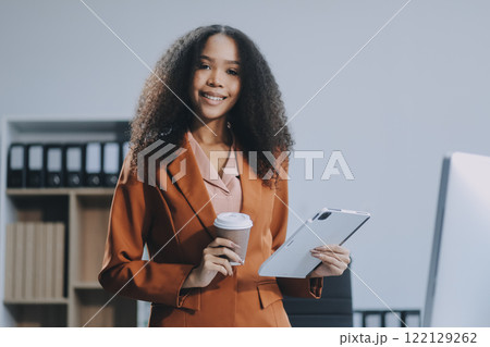 Beautiful young Asian businesswoman smiling holding a coffee mug and laptop working at the office. 122129262