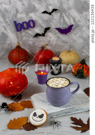 Halloween pumpkin and mug of coffee with cookies on the background of a gray wall with ghosts, bats, spiders, candles, pumpkins. leaves. Selective focus. 122130439