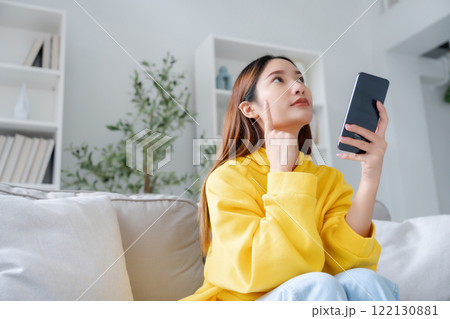 Happy young asian woman relax on comfortable couch at home texting messaging on smartphone 122130881