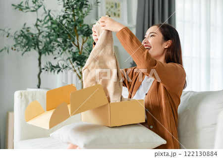 Happy young Asian woman opening delivery package at home Happy young Asian woman opening delivery package at home 122130884