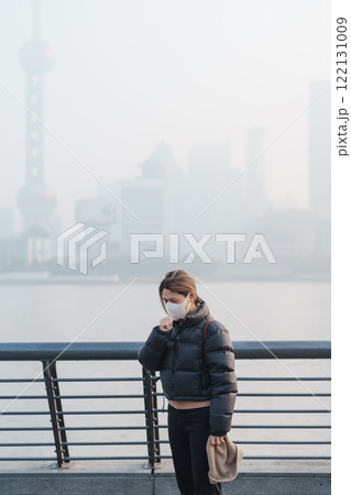 young Asian woman wearing respiratory mask protect and filter pm or particulate matter against bad Air Pollution in Shanghai City, China. Air Quality Index, AQI, Unhealthy, healthcare concept young Asian woman wearing respiratory mask protect and filter pm or particulate matter against bad Air Pollution in Shanghai City, China. Air Quality Index, AQI, Unhealthy, healthcare concept 122131009