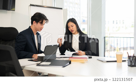 Two smart and professional Asian businesspeople are meeting in a meeting room, planning a project. Two smart and professional Asian businesspeople are meeting in a meeting room, planning a project. 122131507