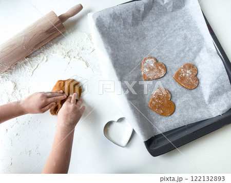 Child making heart shaped cookies on baking tray with rolling pin and cookie cutter 122132893