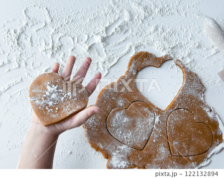 Childs hand holding heart shaped cookie with flour on table 122132894