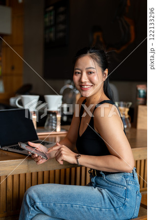 An attractive Asian woman sits at a counter bar in a coffee shop with her laptop, working remotely. An attractive Asian woman sits at a counter bar in a coffee shop with her laptop, working remotely. 122133296