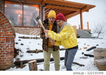 Older husband teaching his wife how to cut wood. He is preparing logs for the fireplace. 122135349