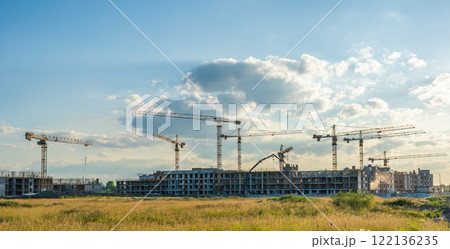 Construction cranes erecting residential buildings against sunset sky with cloudy backdrop 122136235