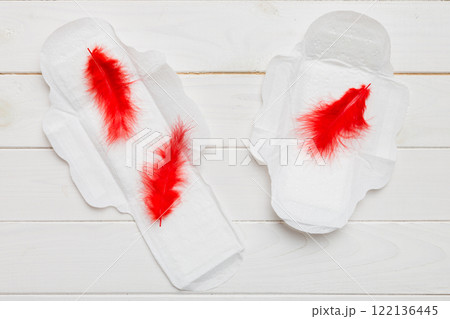 Women hygiene products or Sanitary pad with red feather on colored background. Pastel color. Closeup. Empty place for text. Female daily hygiene Women hygiene products or Sanitary pad with red feather on colored background. Pastel color. Closeup. Empty place for text. Female daily hygiene 122136445