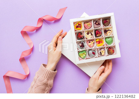 Female hands with delicious candies in box on color background Female hands with delicious candies in box on color background 122136482