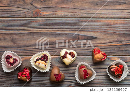 chocolate sweets in the form of a heart with fruits and nuts on a colored background. top view with space for text, holiday concept chocolate sweets in the form of a heart with fruits and nuts on a colored background. top view with space for text, holiday concept 122136497