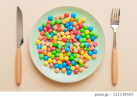 cutlery on table and sweet plate of candy. Health and obesity concept, top view on colored background 122136505
