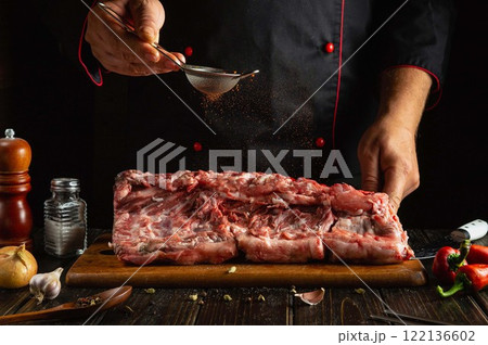 Expertly slicing and seasoning a large cut of meat, the chef enhances flavors with spices while surrounded by ingredients. The warm kitchen atmosphere invites culinary creativity Expertly slicing and seasoning a large cut of meat, the chef enhances flavors with spices while surrounded by ingredients. The warm kitchen atmosphere invites culinary creativity 122136602
