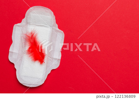 Women hygiene products or Sanitary pad with red feather on colored background. Pastel color. Closeup. Empty place for text. Female daily hygiene Women hygiene products or Sanitary pad with red feather on colored background. Pastel color. Closeup. Empty place for text. Female daily hygiene 122136809