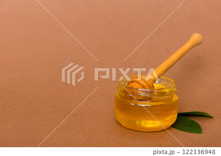 Honey in jar with leaves and honey dipper on colored background top view with copy text 122136948