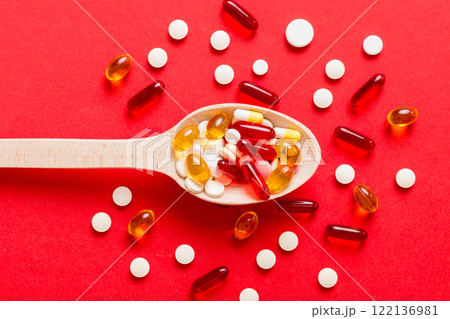 Vitamin capsules in a spoon on a colored background. Pills served as a healthy meal. Red soft gel vitamin supplement capsules on spoon Vitamin capsules in a spoon on a colored background. Pills served as a healthy meal. Red soft gel vitamin supplement capsules on spoon 122136981