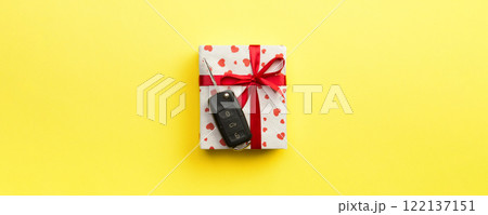 Car key on paper gift box with red ribbon bow and heart on yellow table background. Holidays present top view concept Car key on paper gift box with red ribbon bow and heart on yellow table background. Holidays present top view concept 122137151