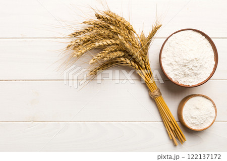 Flat lay of Wheat flour in wooden bowl with wheat spikelets on colored background. world wheat crisis Flat lay of Wheat flour in wooden bowl with wheat spikelets on colored background. world wheat crisis 122137172