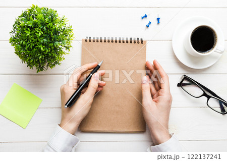 Woman hand with pencil writing on notebook and hold coffee cup. Woman working on office table with coffee Woman hand with pencil writing on notebook and hold coffee cup. Woman working on office table with coffee 122137241