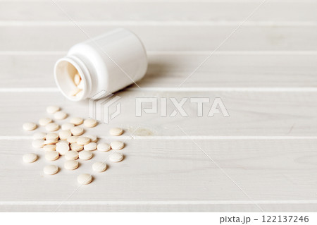 Medicine bottle and white pills spilled on a light background. Medicines and prescription pills flat lay background. White medical pills and tablets spilling out of a drug bottle Medicine bottle and white pills spilled on a light background. Medicines and prescription pills flat lay background. White medical pills and tablets spilling out of a drug bottle 122137246