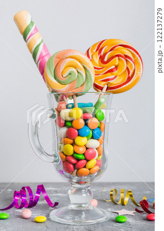 Colorful candies in cup on table on light background background. Large swirled lollipops. Creative concept of a jar full of delicious sweets from the candy store Colorful candies in cup on table on light background background. Large swirled lollipops. Creative concept of a jar full of delicious sweets from the candy store 122137279