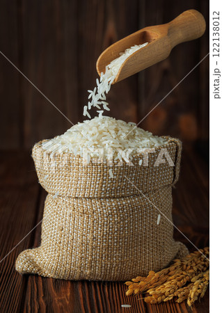 rice falling from scoop in sack with ears near on wooden background 122138012
