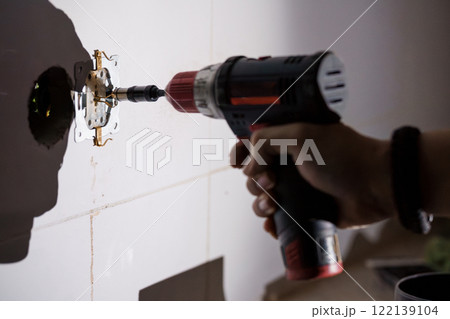 Electric Drill In Use for Installing Electrical Outlet on Wall 122139104