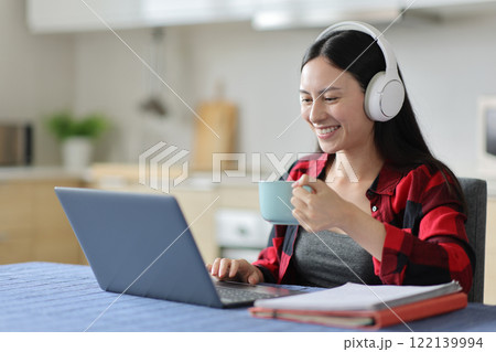 Happy asian student using headphone and laptop in the kitchen 122139994