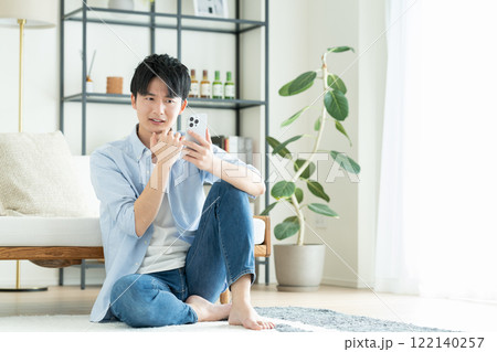 リビングでスマホを見る若い男性 122140257