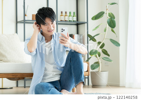 リビングでスマホを見る若い男性 122140258