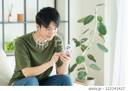 リビングでスマホを見る若い男性 122141427