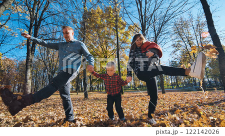 Family spending autumn afternoon walking through fallen leaves, laughing and playing together in golden hued park landscape Family spending autumn afternoon walking through fallen leaves, laughing and playing together in golden hued park landscape 122142026