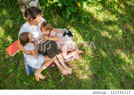 Mom and kids relaxing together on a blanket with their dog outdoors 122142117