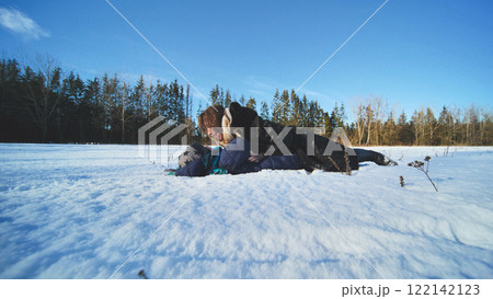 Mother and her son are lying on a snow covered field, cuddling and having fun on a beautiful winter day 122142123