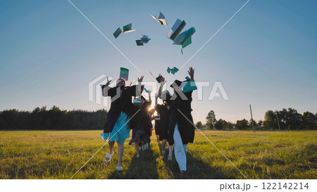 Happy graduates tossing their books in the air and running through a field at sunset Happy graduates tossing their books in the air and running through a field at sunset 122142214