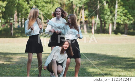 Four cheerful schoolgirls in uniform celebrating their first school day, dancing and having fun together in a park Four cheerful schoolgirls in uniform celebrating their first school day, dancing and having fun together in a park 122142247