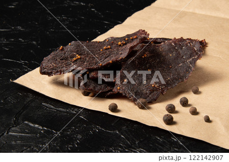 Veal jerky on craft paper and black background. Veal jerky on craft paper and black background. 122142907